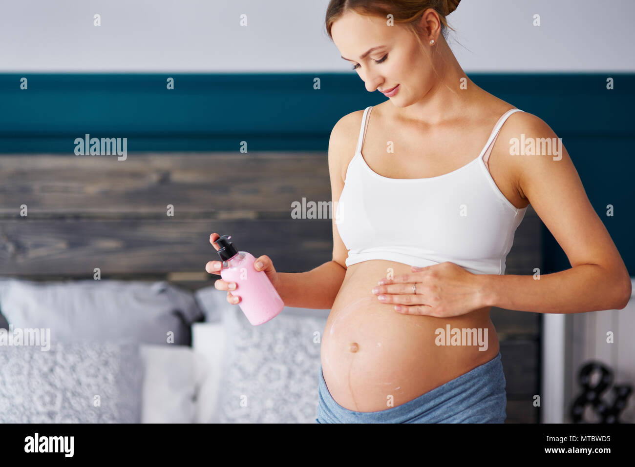Young pregnant women applying cream on her belly Stock Photo