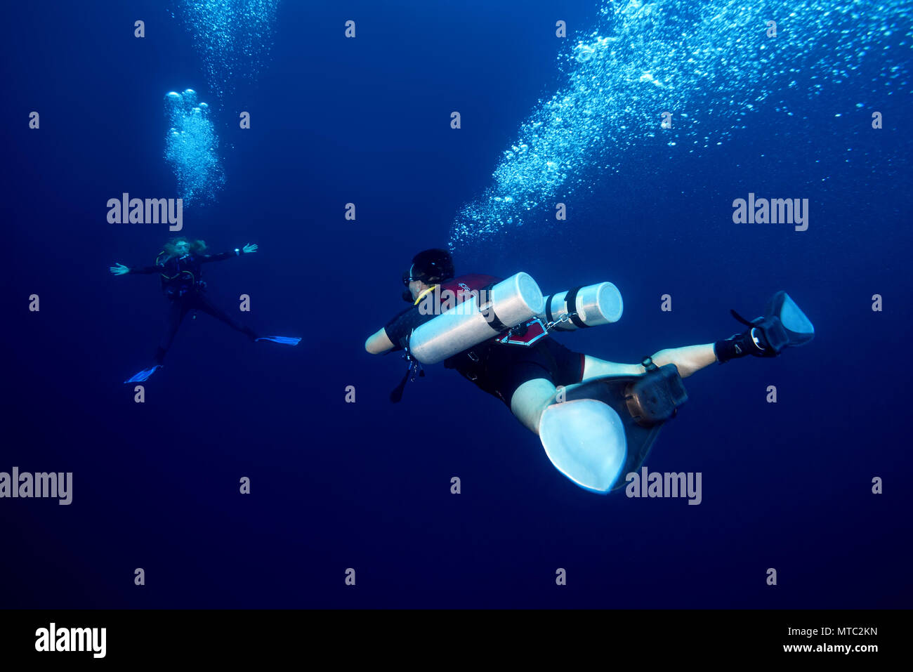 Two scuba divers man with sidemount and woman hungs in the blue water and waits passes decompression time on safety stop Stock Photo