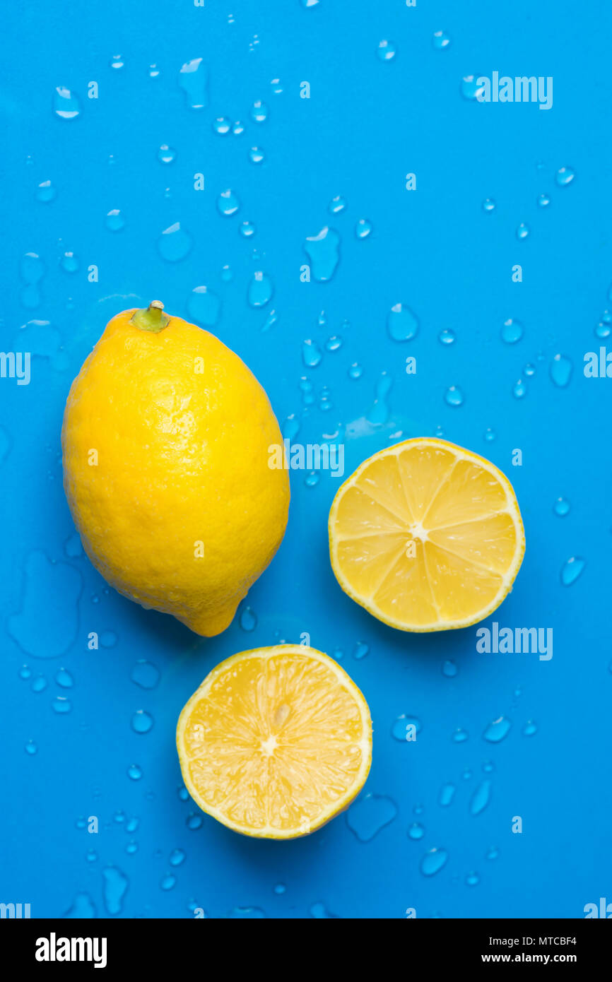 Ripe Juicy Whole and Sliced Lemon on Blue Background with Water Drops. Vitamins Healthy Diet Summer Superfoods Concept. Copy Space Poster Banner Templ Stock Photo