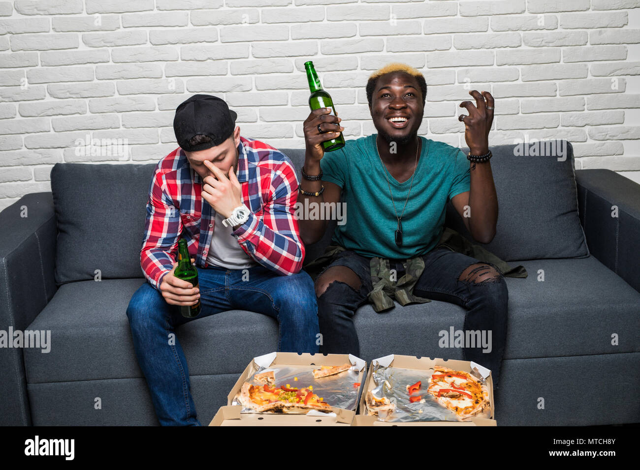 Domestic life. Two young mixed race men watching a football match on tv  with different emotiond of win and lose. Sport fans Stock Photo - Alamy