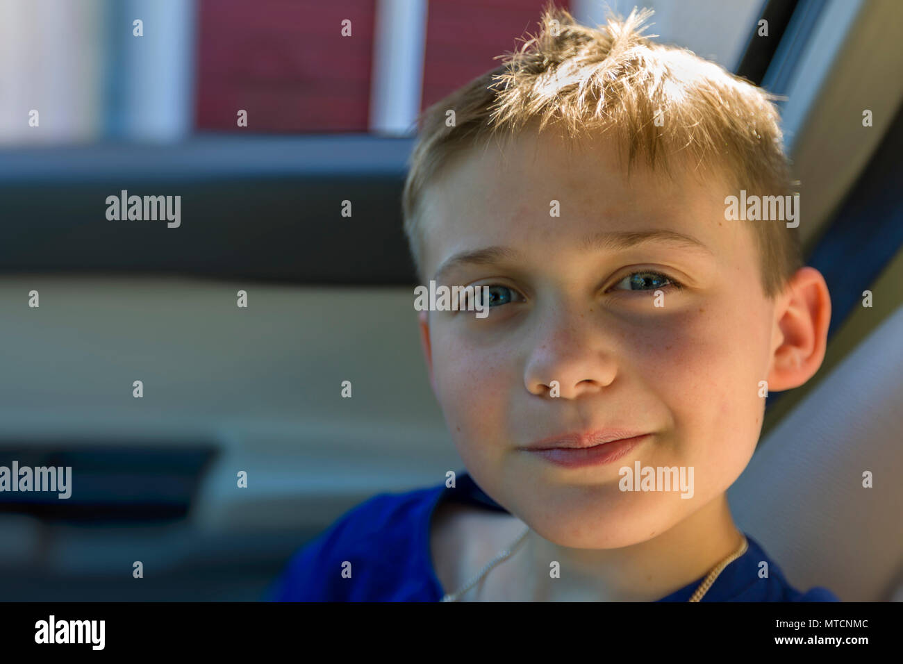 Close up view portrait of cute young 10 year old caucasian boy in car passenger seat looking and smiling at camera Stock Photo