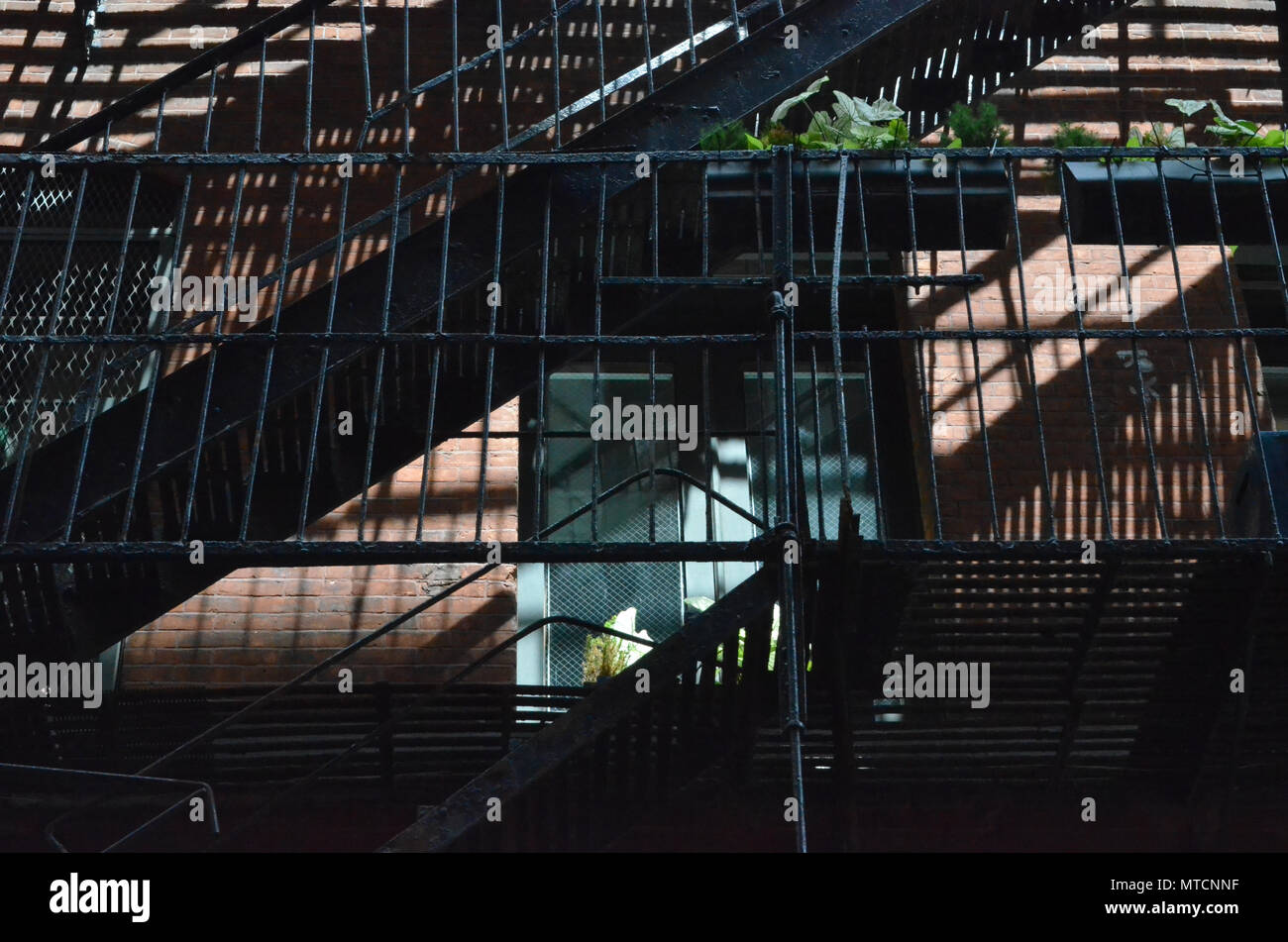 A black fire escape, shadows, and a window on an old industrial brick building in New Yorkâ€™s Soho distruct Stock Photo