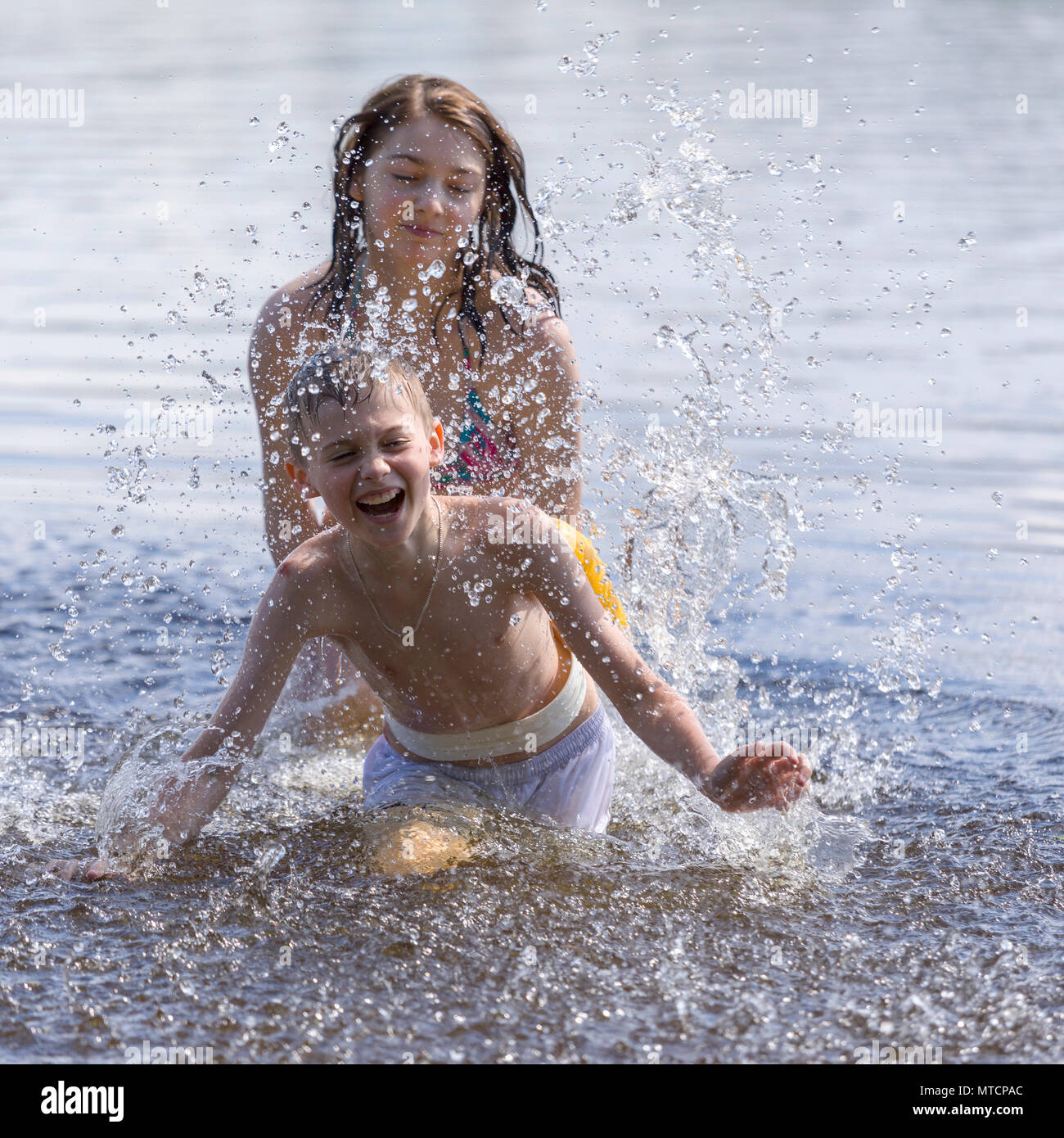 Young boy and girl, sister and brother, siblings having fun, playing in the water in a lake in the summer Stock Photo
