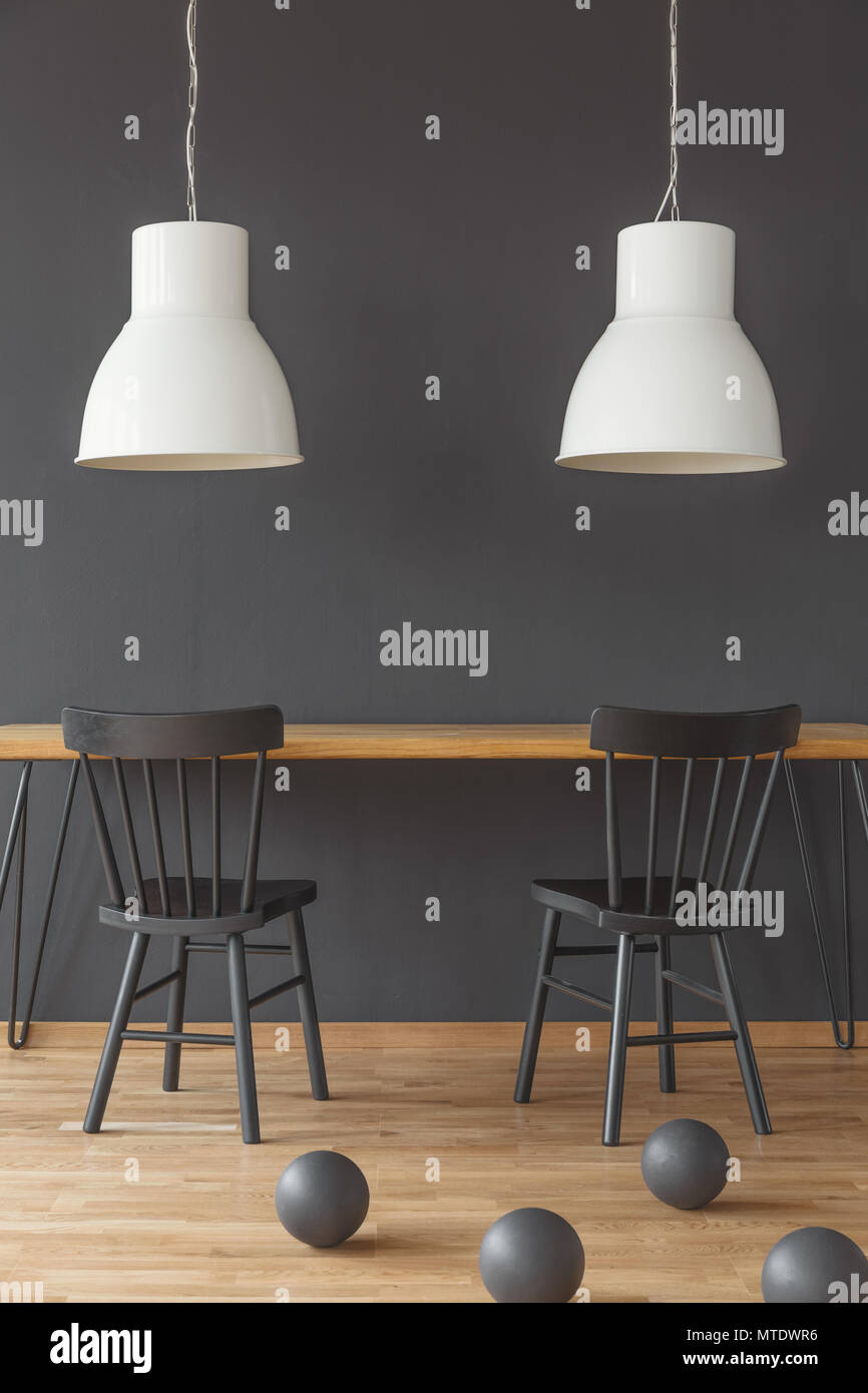 Black chairs at wooden table under white lamps in dining room interior with balls Stock Photo
