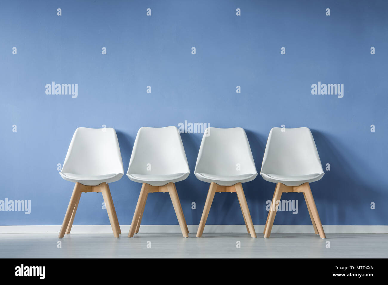 Front View Of A Row Of Modern Simple White Chairs Against Blue Wall In A Minimal Style Waiting Room Interior Stock Photo Alamy