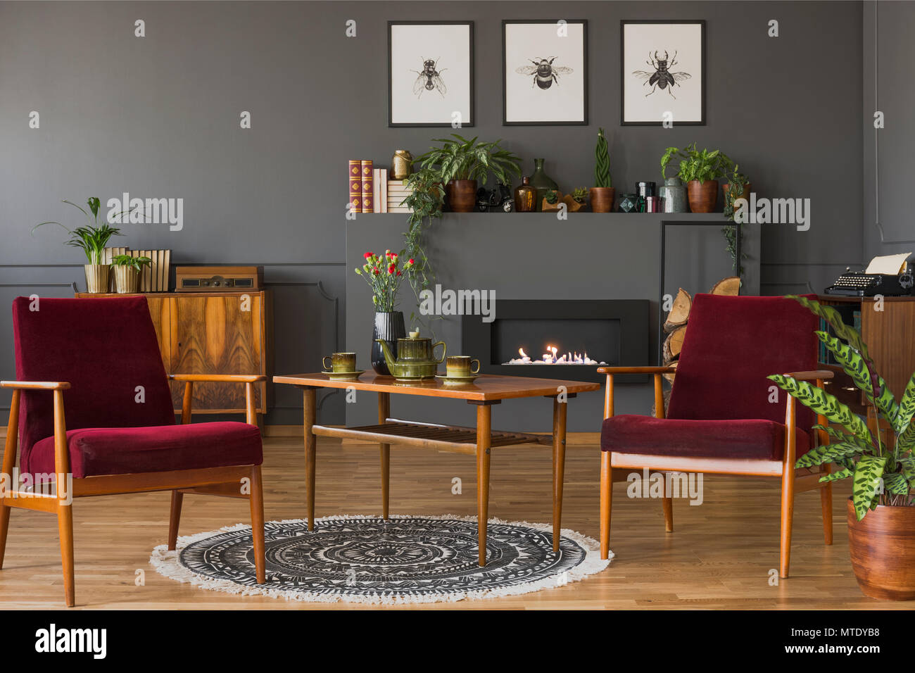 Dark red wooden armchairs in vintage flat interior with posters on grey wall above fireplace. Real photo Stock Photo