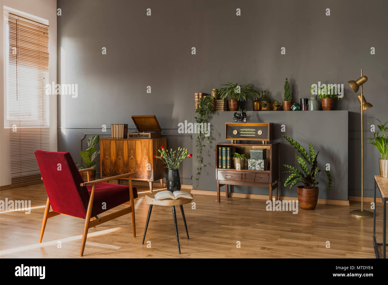 Dark red armchair next to table with flowers in grey vintage flat interior  with radio on cabinet. Real photo Stock Photo - Alamy