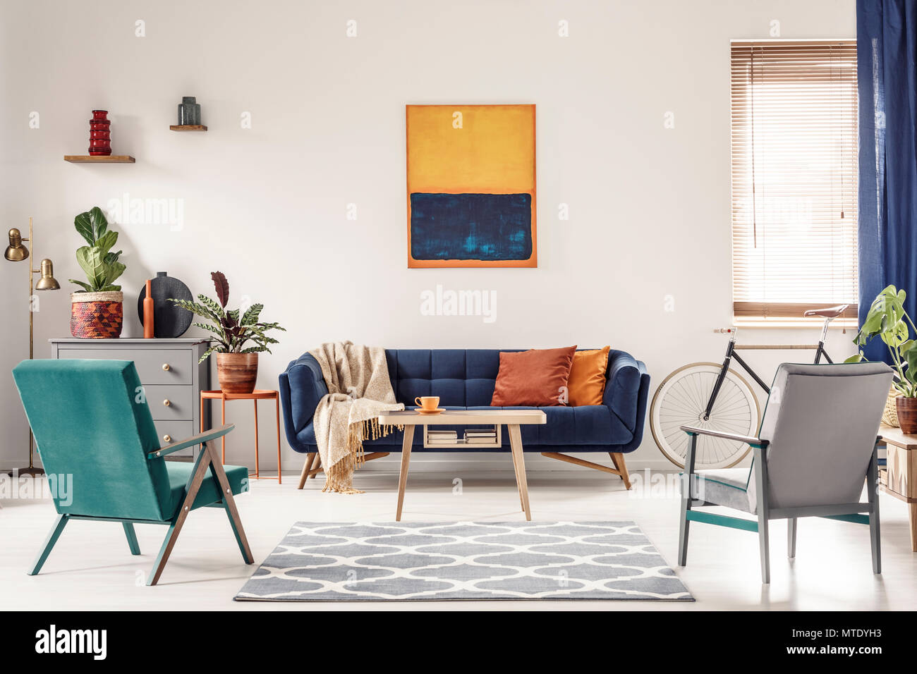 Real photo of a navy blue sofa with orange cushions and an artwork above in  bright and spacious living room interior with two retro armchairs Stock  Photo - Alamy