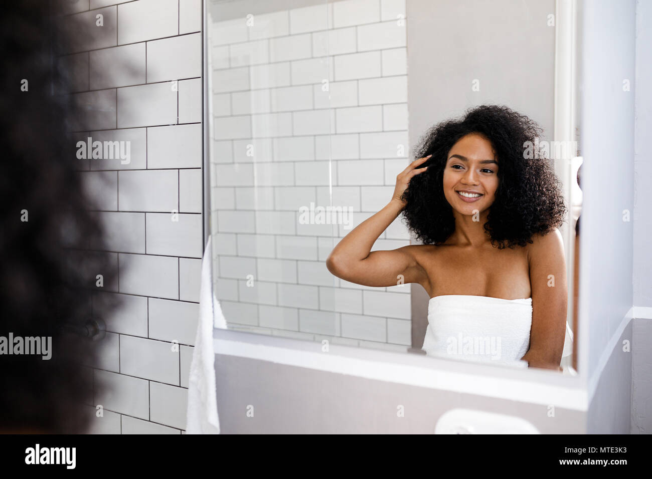 Shot of a young smiling woman deciding on a hair style in front of a mirror Stock Photo