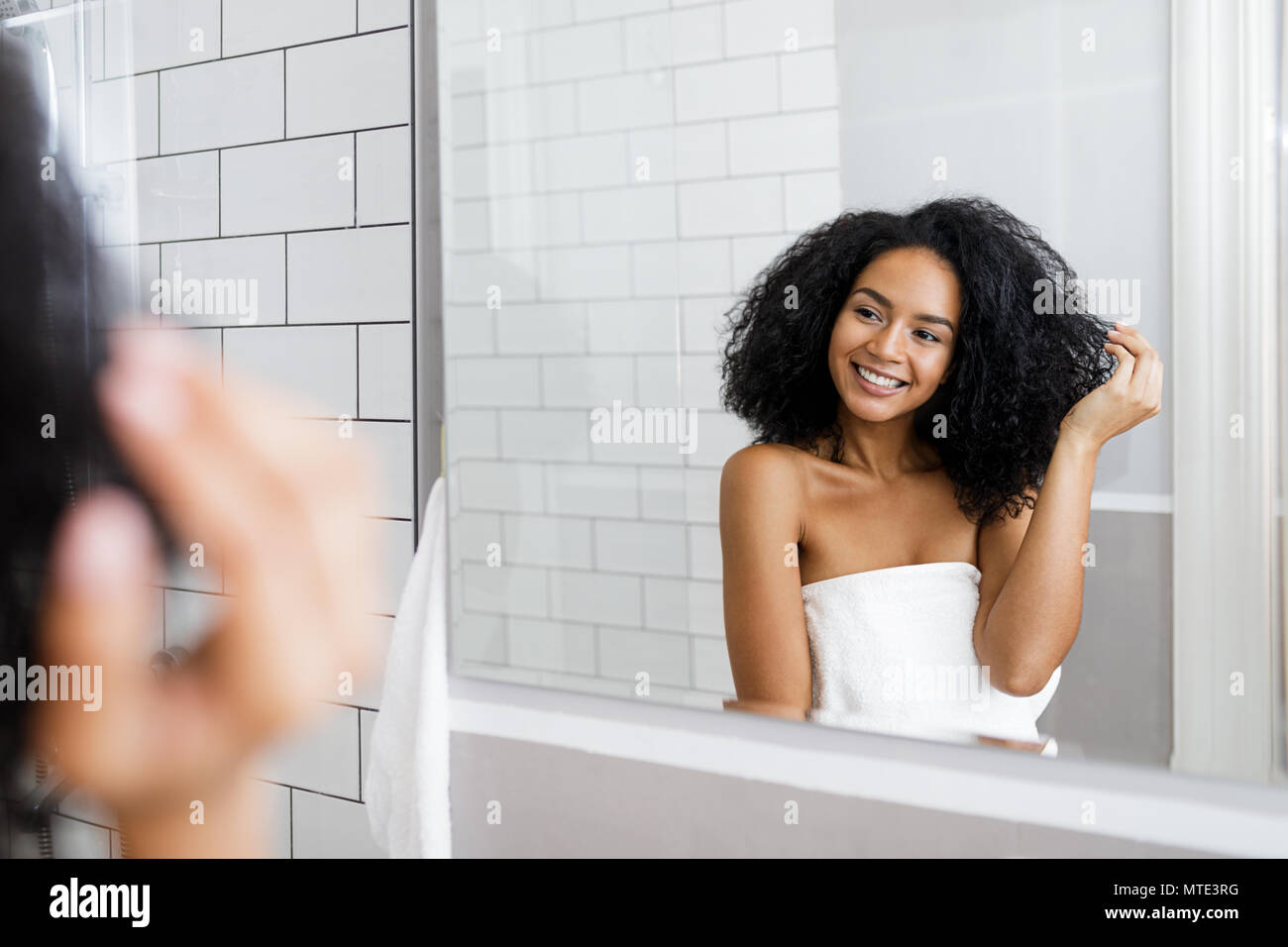 Young woman standing in bathroom, holding her curly hair Stock Photo