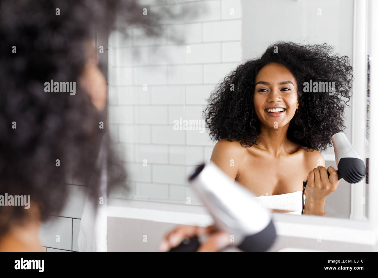 A young woman blow drying her hair in front of a mirror Stock Photo - Alamy