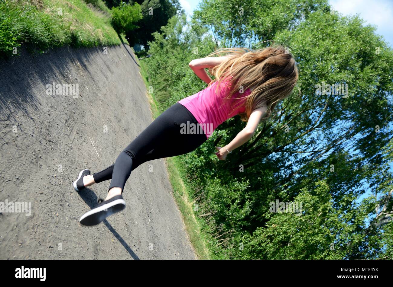 Young female runner. Woman runs on dirt road surrounded by green trees. Photo from behind, without face. Stock Photo
