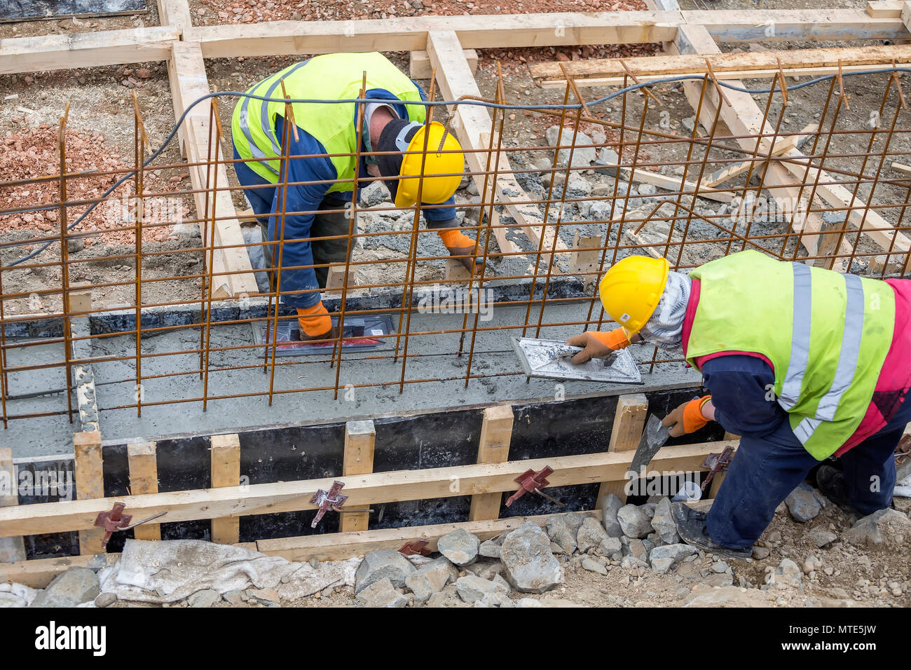 Builders crew leveling concrete footing pour with rebar and formwork