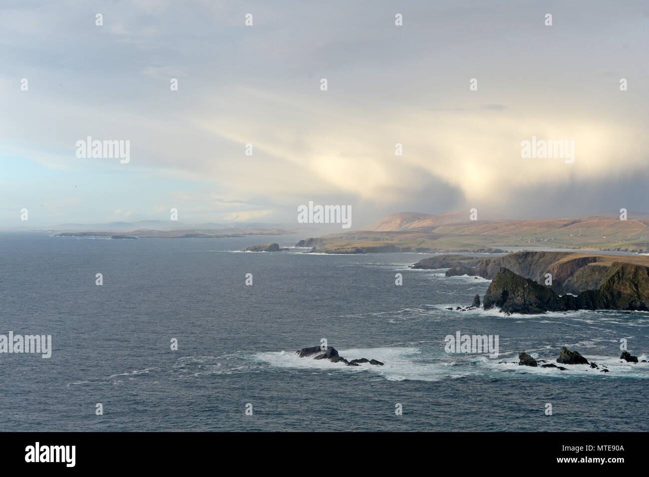 High up cliff shots of the sea and land in Shetland with a storm and a rainbow and choppy seas Stock Photo