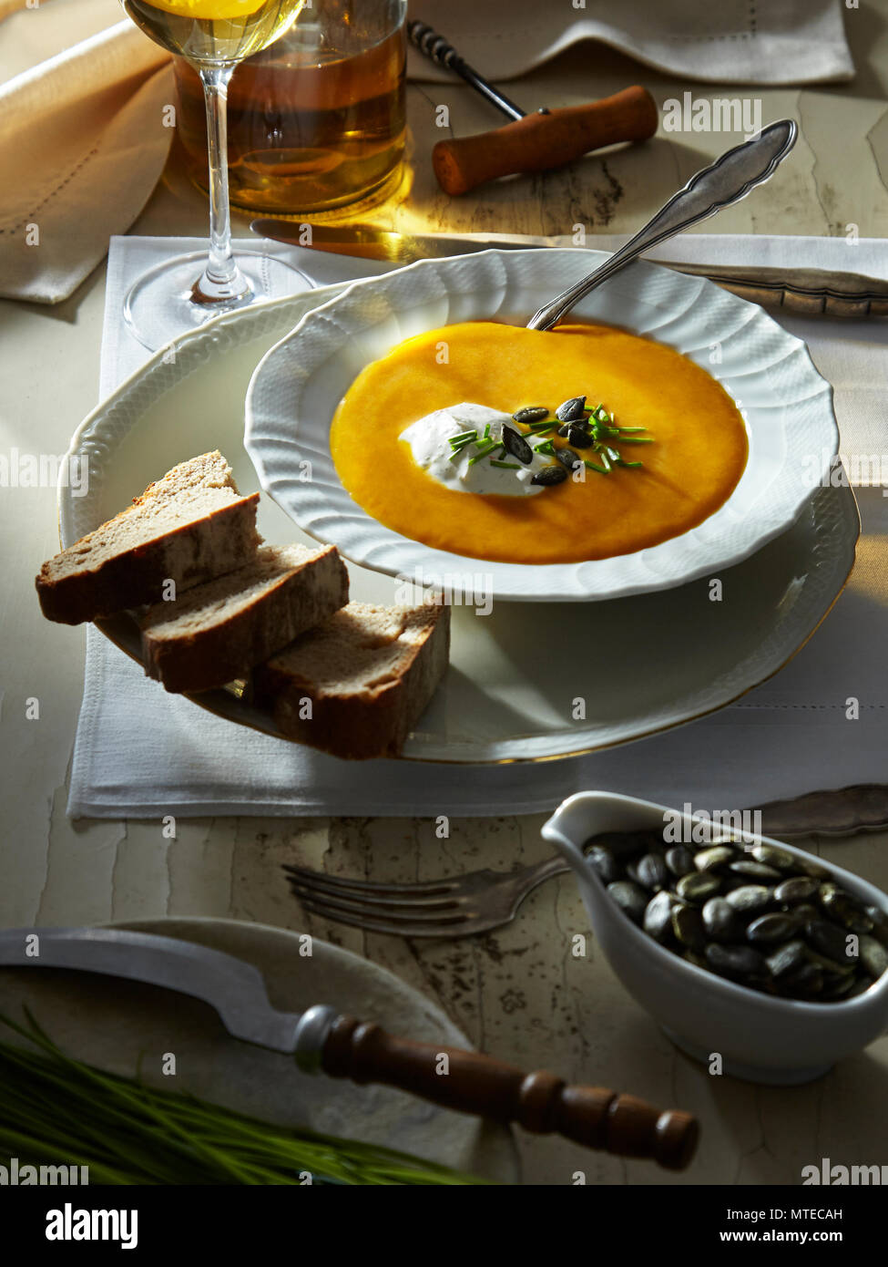 Kürbissuppe mit Kürbiskernen, Brot und Crème fraîche, gedeckter Tisch Stock Photo