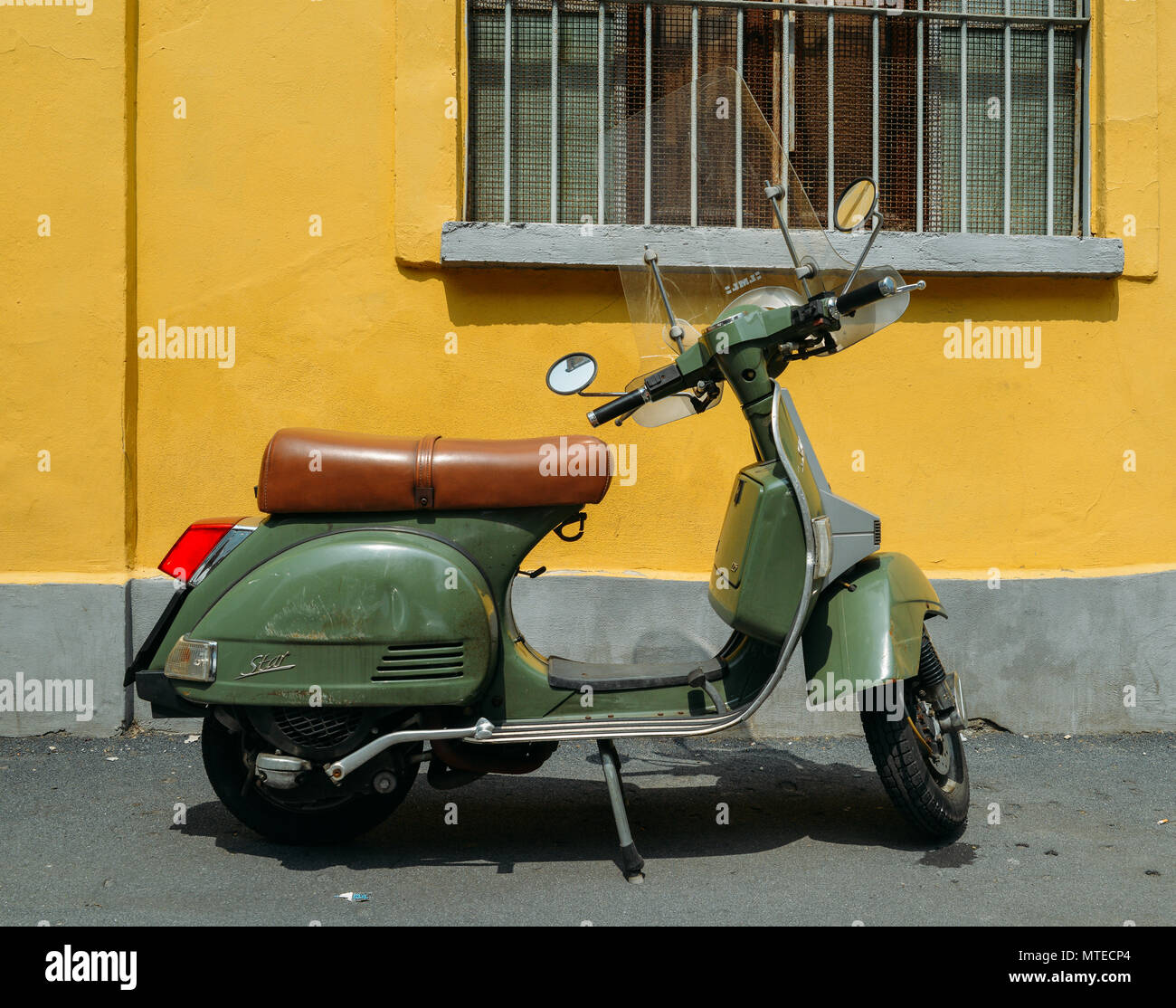 Green Piaggio Vespa LML T5 150 parked on side of street with yellow background Stock Photo