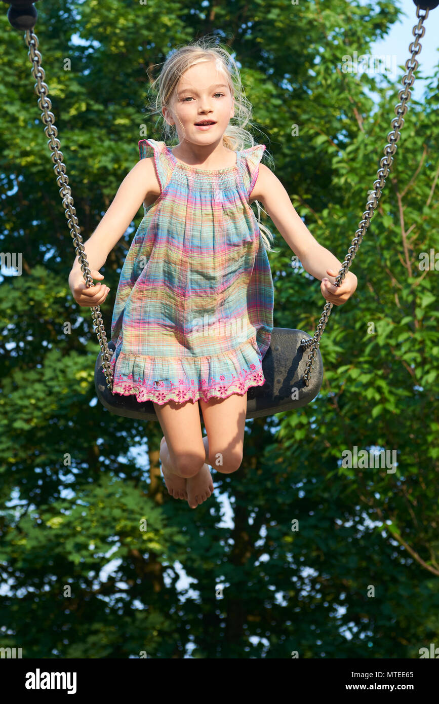 Little child blond girl having fun on a swing outdoor. Summer ...