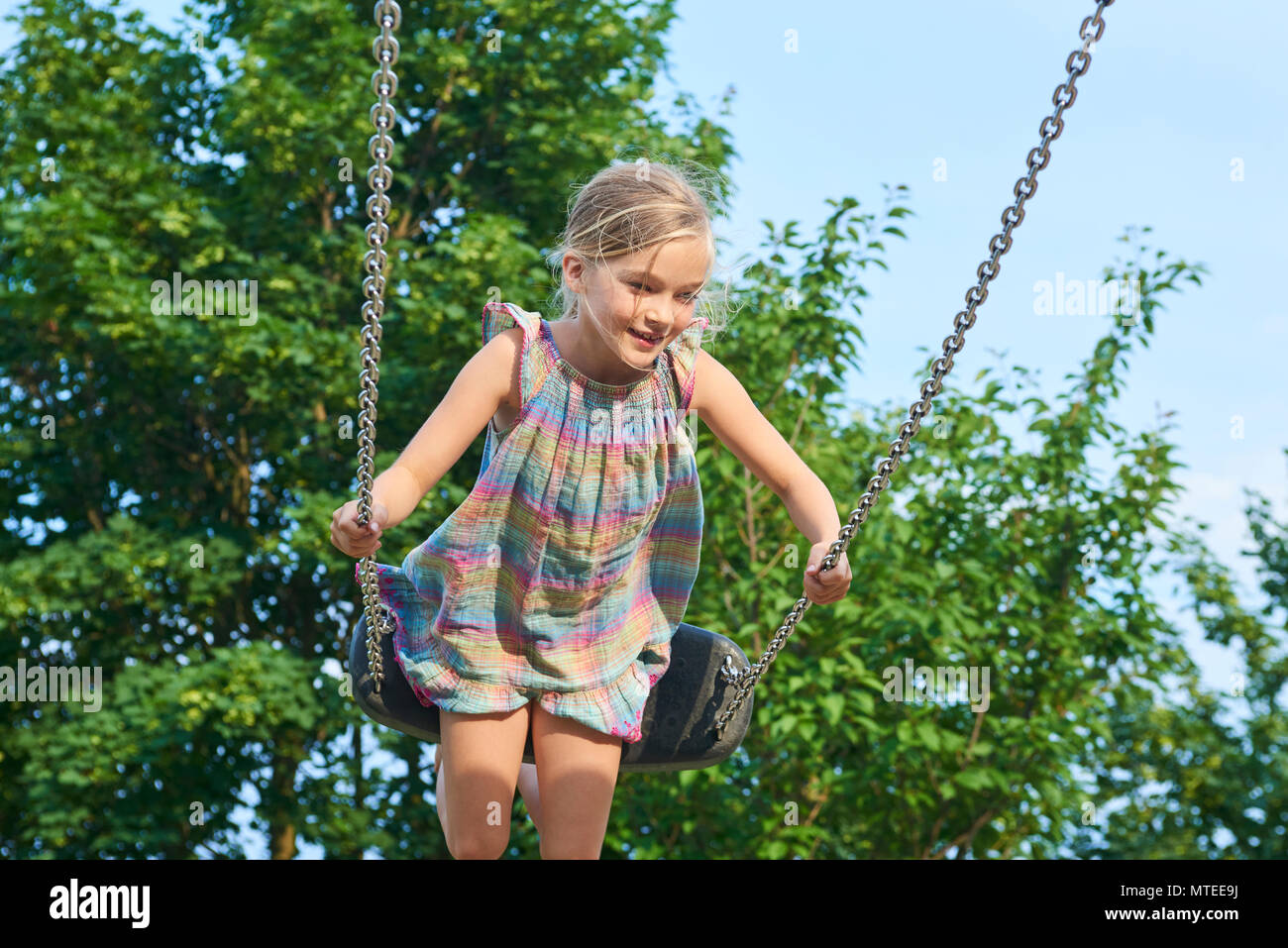 Little child blond girl having fun on a swing outdoor. Summer ...