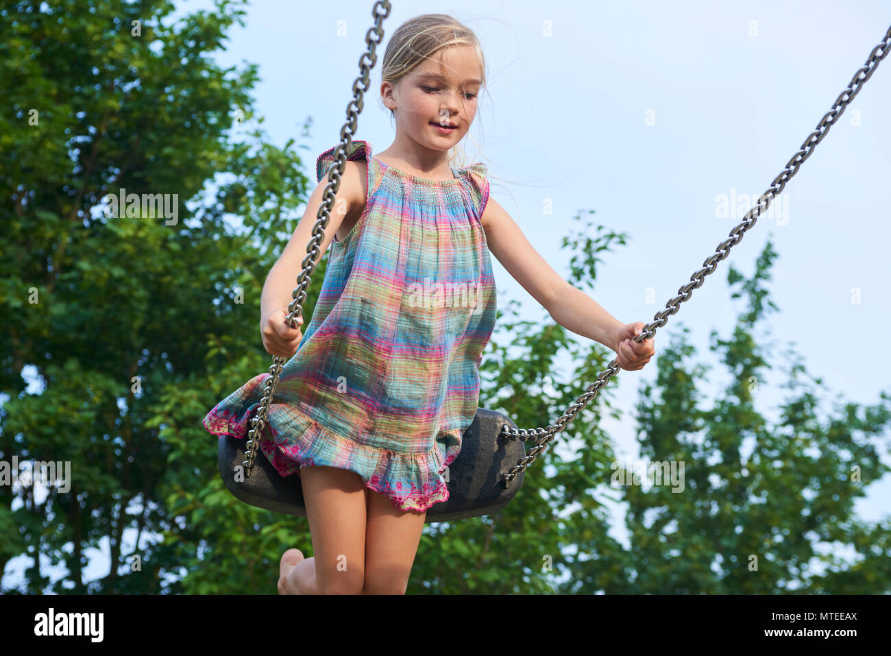 Little child blond girl having fun on a swing outdoor. Summer playground. Girl swinging high. Young child on swing outdoors. Stock Photo
