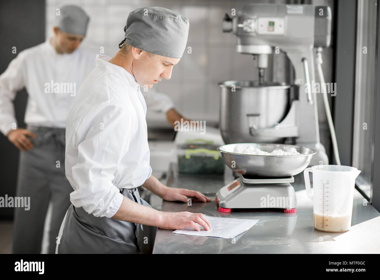 Two handsome male confectioners in uniform weighing ingredients for baking at the manufacturing Stock Photo