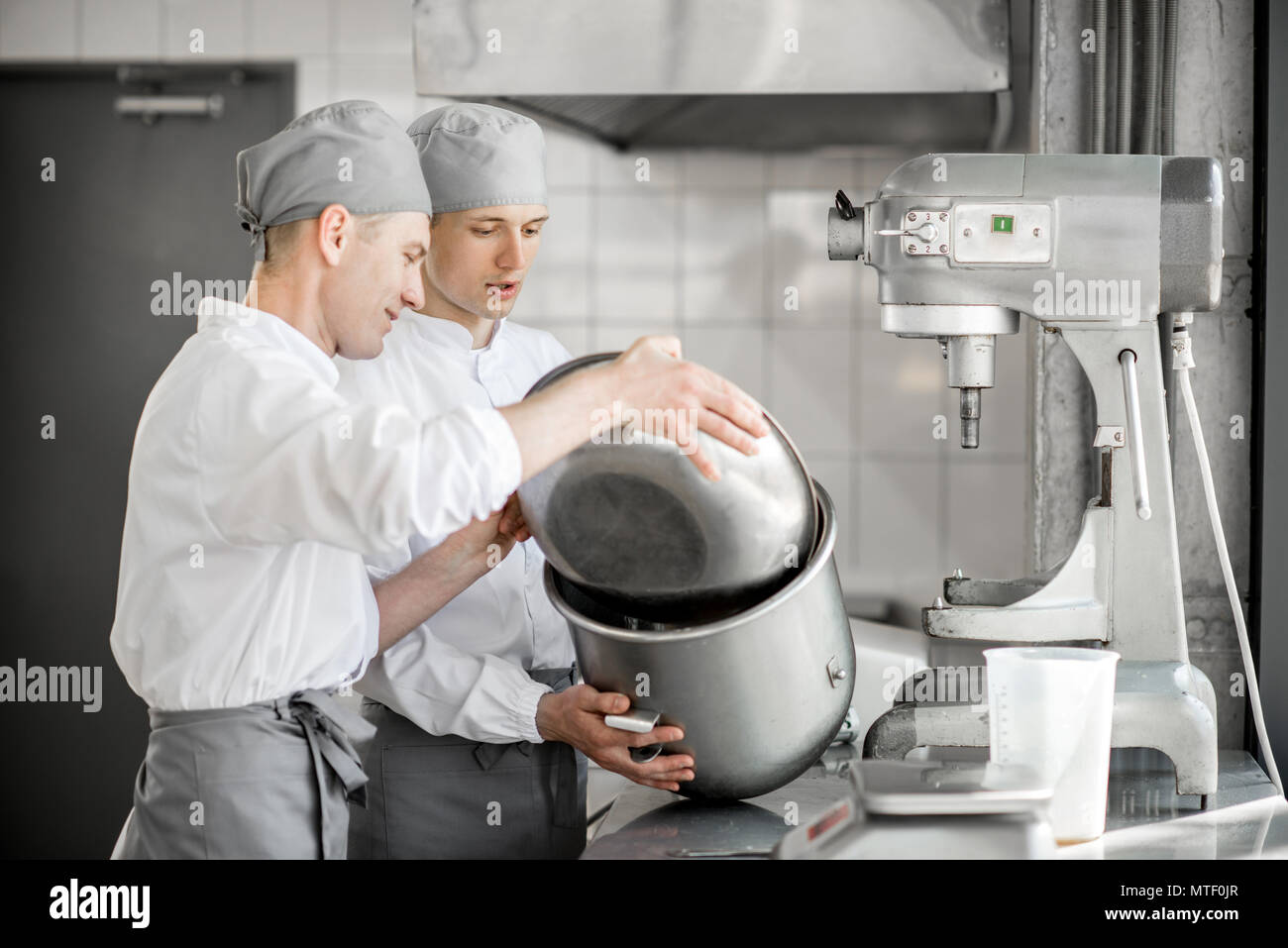 Two handsome confectioners mixing ingredients in bowls for baking at the manufacturing Stock Photo