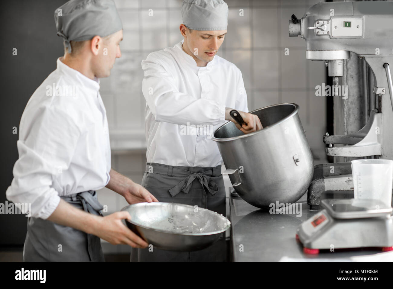 Two handsome confectioners mixing ingredients in bowls for baking at the manufacturing Stock Photo