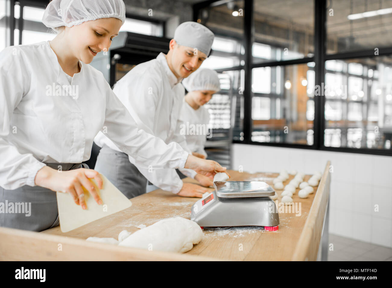 Three bakers having fun forming dough for baking standing together at the modern manufacturing Stock Photo