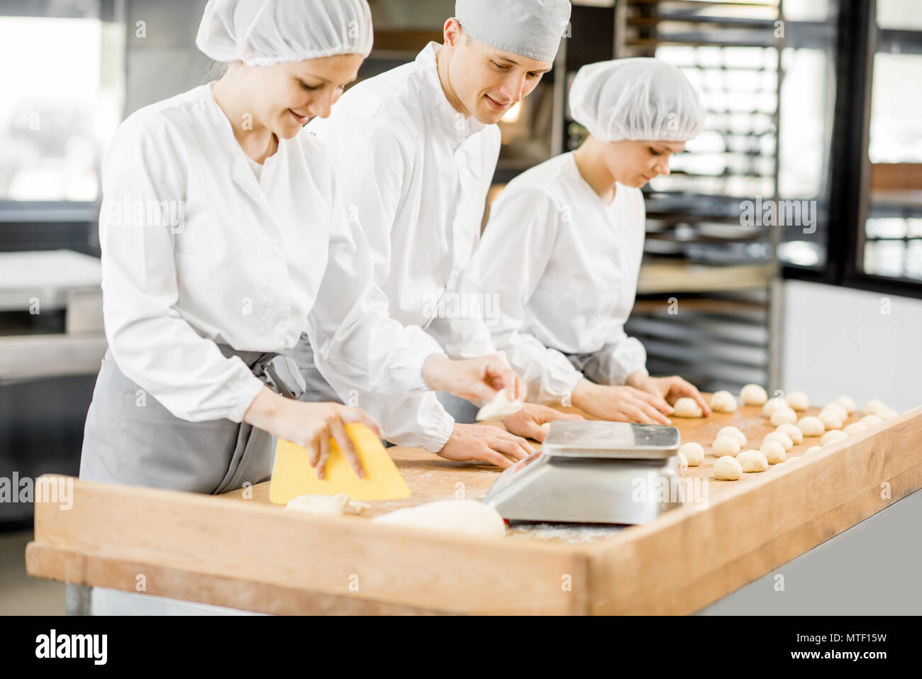 Three bakers having fun forming dough for baking standing together at the modern manufacturing Stock Photo