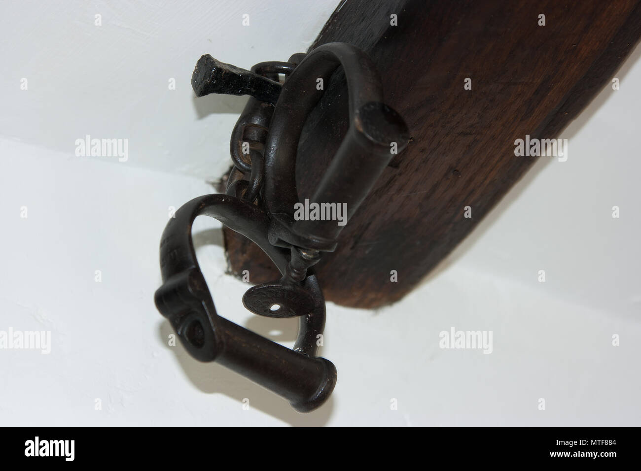 Vintage hand-forged iron handcuffs and key hanging on old oak beam Stock Photo