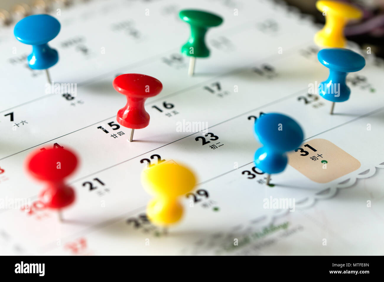 Various color thumb tack pins on calendar as reminder Stock Photo