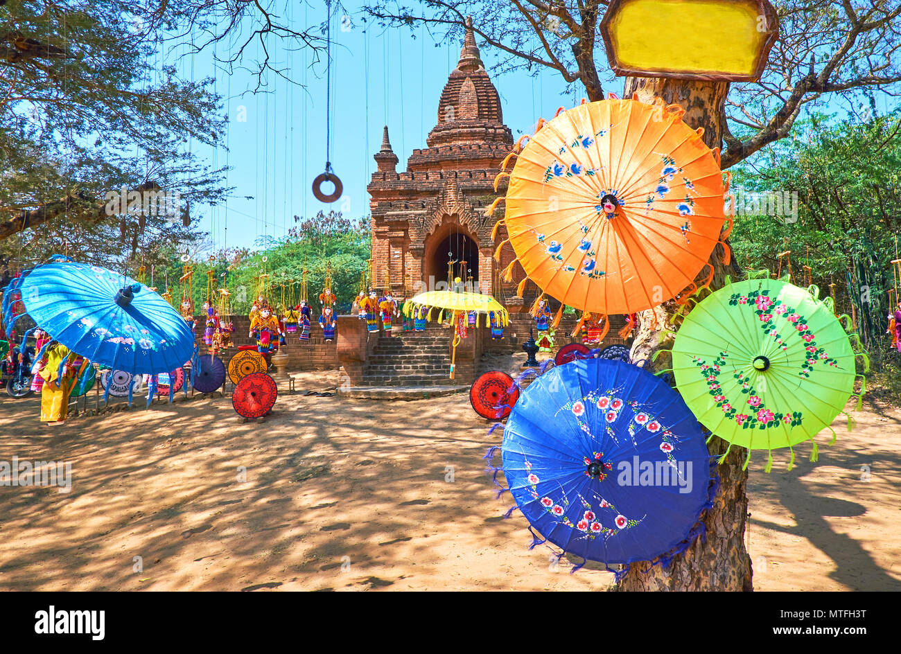Traditional colored umbrellas and beautiful dolls are hanging on the tree next to the ancient Buddhist Shrine in archaeological site, Bagan, Myanmar Stock Photo