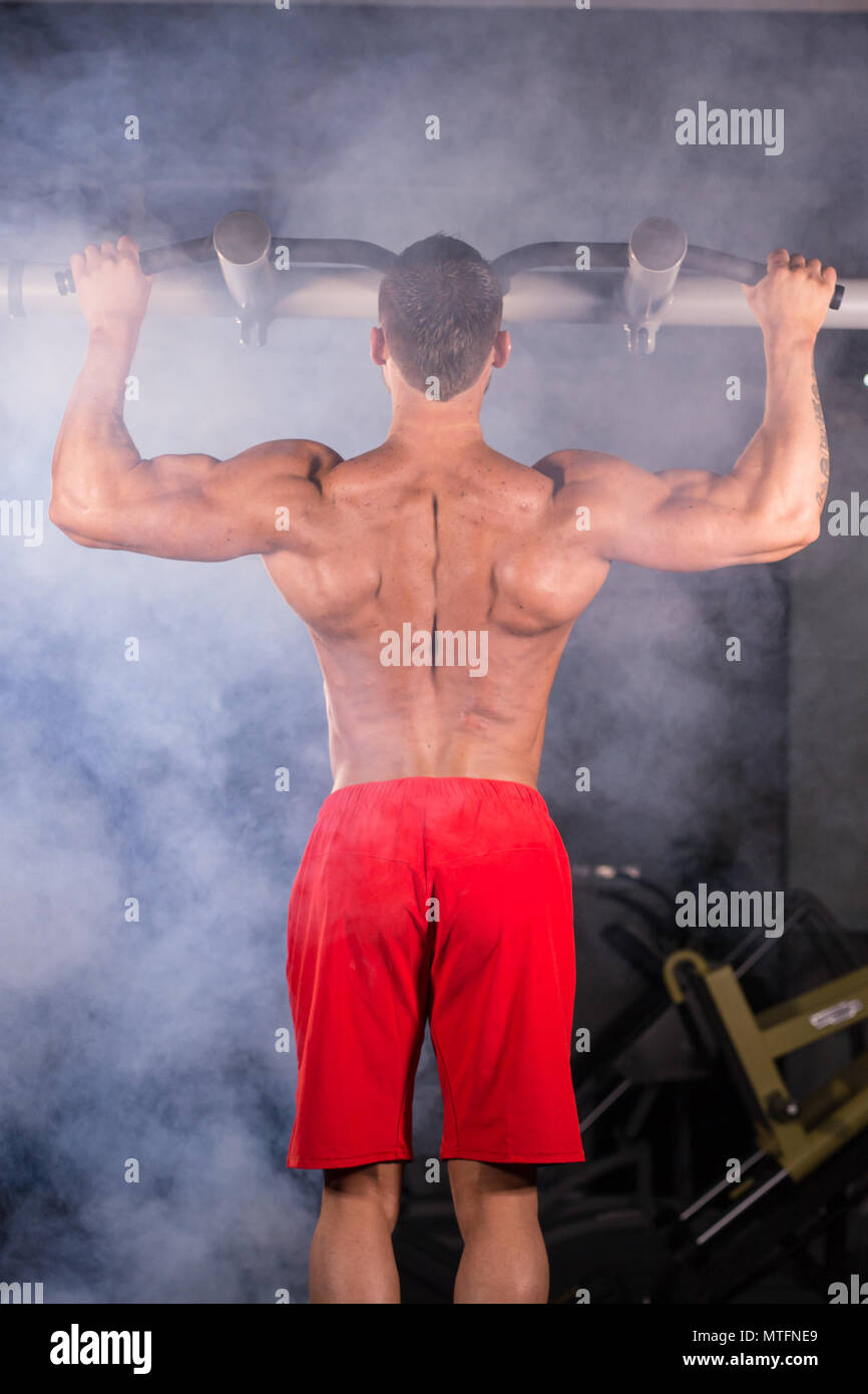 Strong young man doing pull up exercise on horizontal bar in gym ...