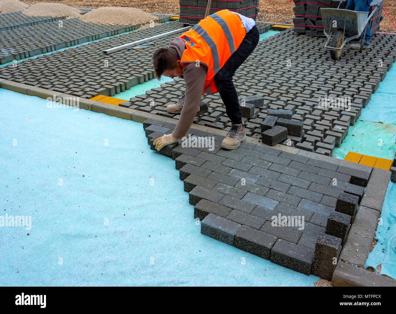 Construction worker laying interlocking paving concrete onto sheet