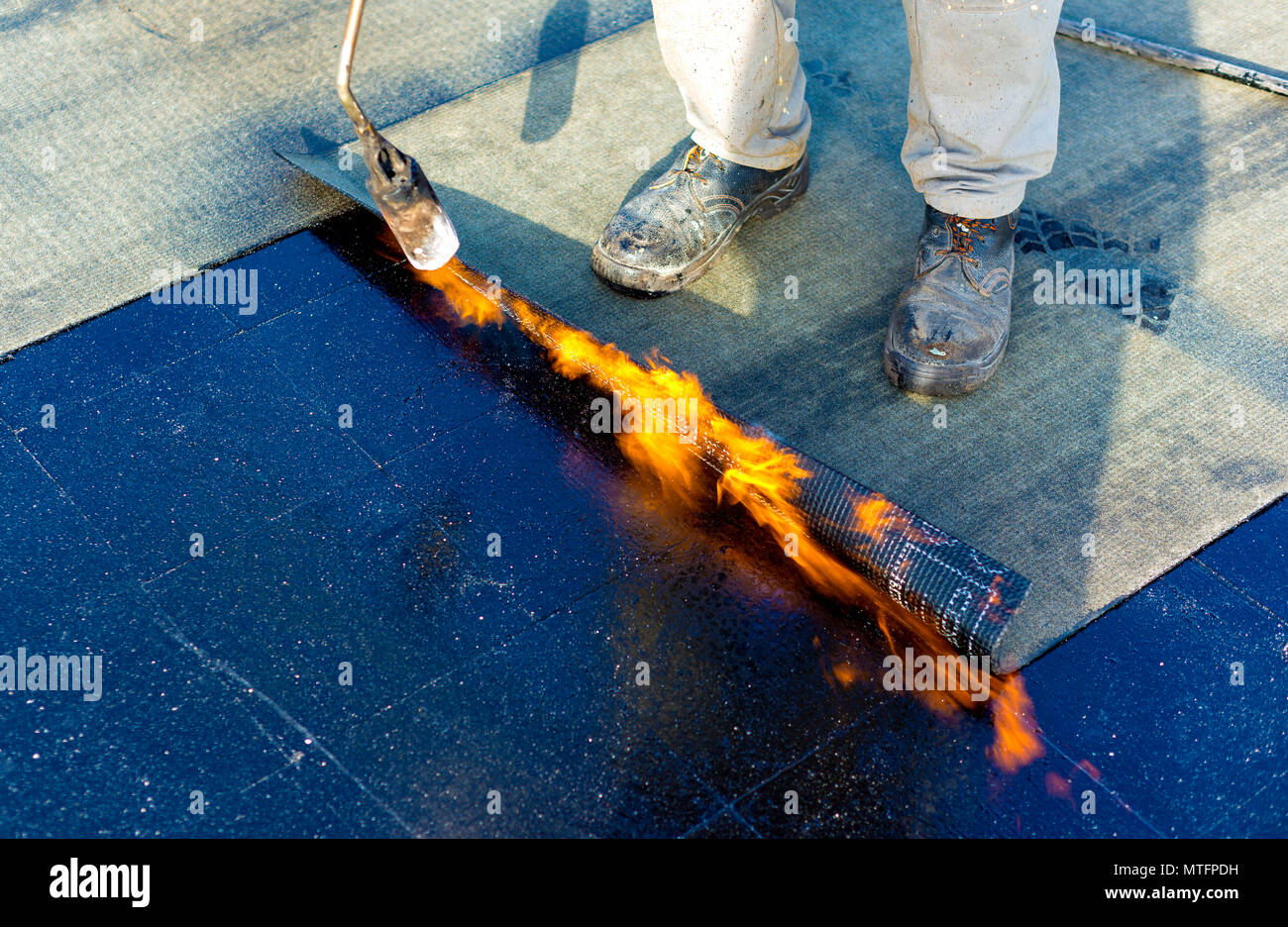 Worker preparing part of bitumen roofing felt roll for melting by gas heater torch flame Stock Photo