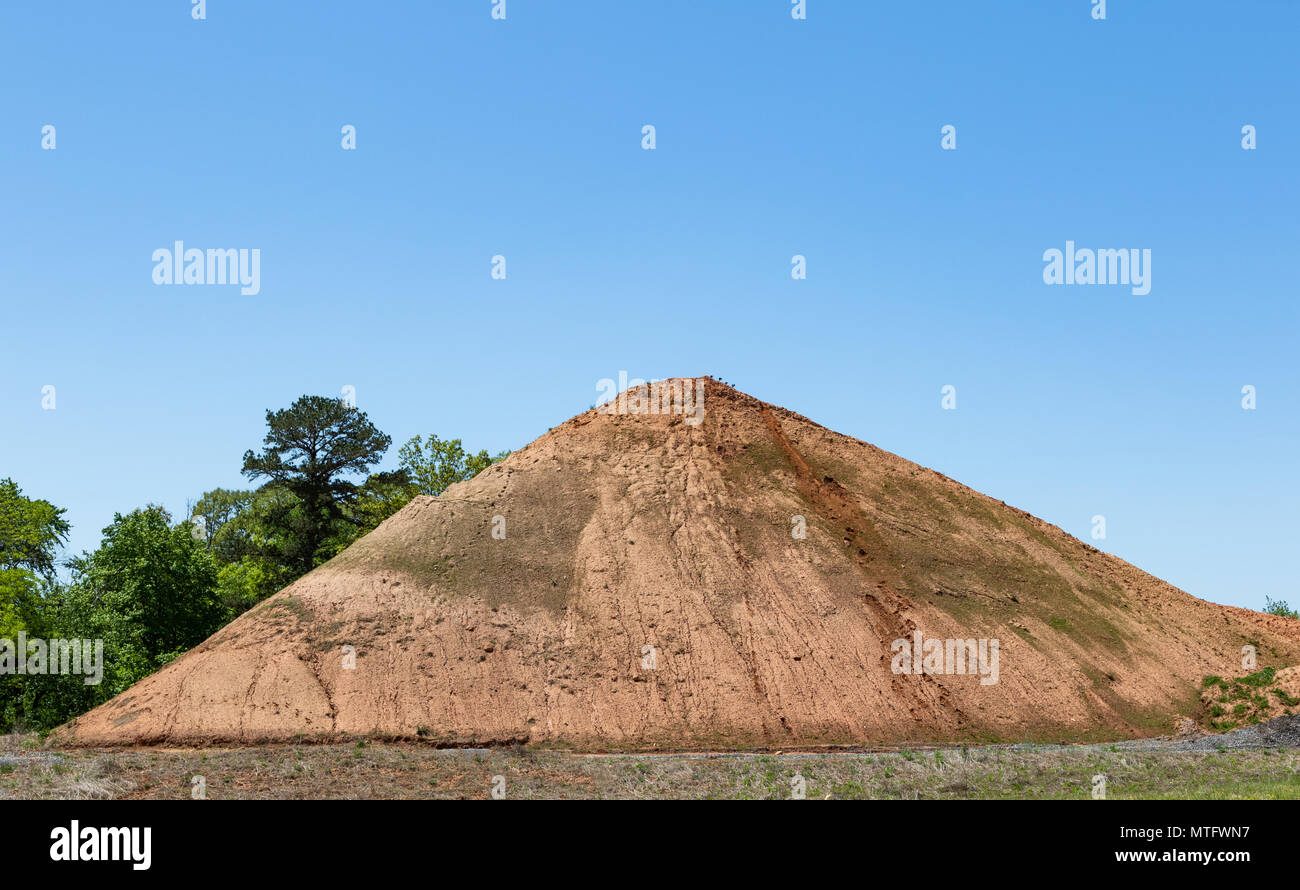 A large pyramid-shaped pile of dirt, framed on left side by green trees.  Text space. Stock Photo