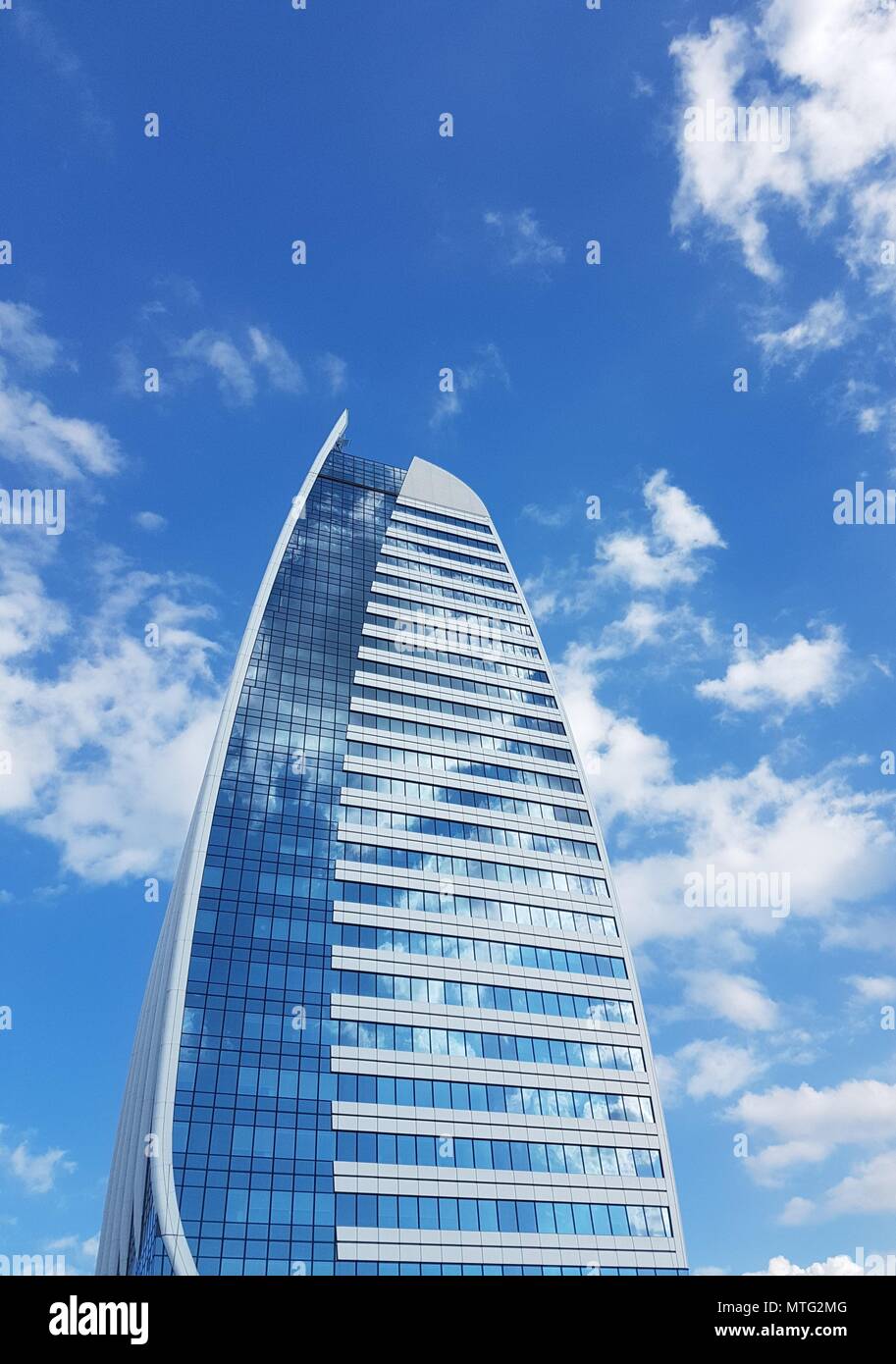 Tall office building with windows reflecting the sky with white clouds Stock Photo