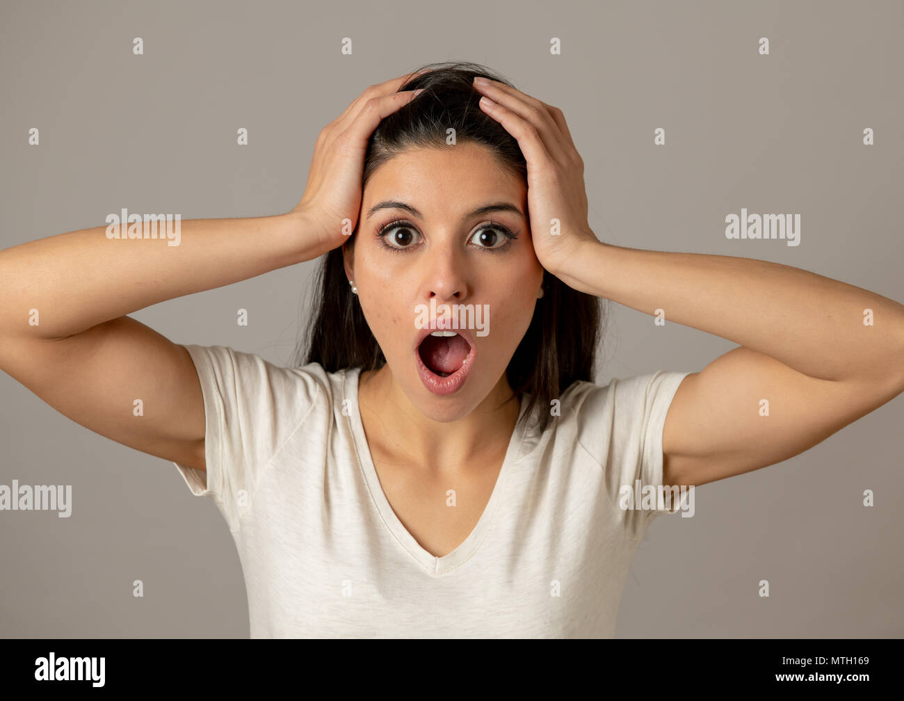 Close up portrait of a beautiful young latin hispanic woman with a surprised and shocked face looking amazed with wide eyes and mouth open.Human facia Stock Photo