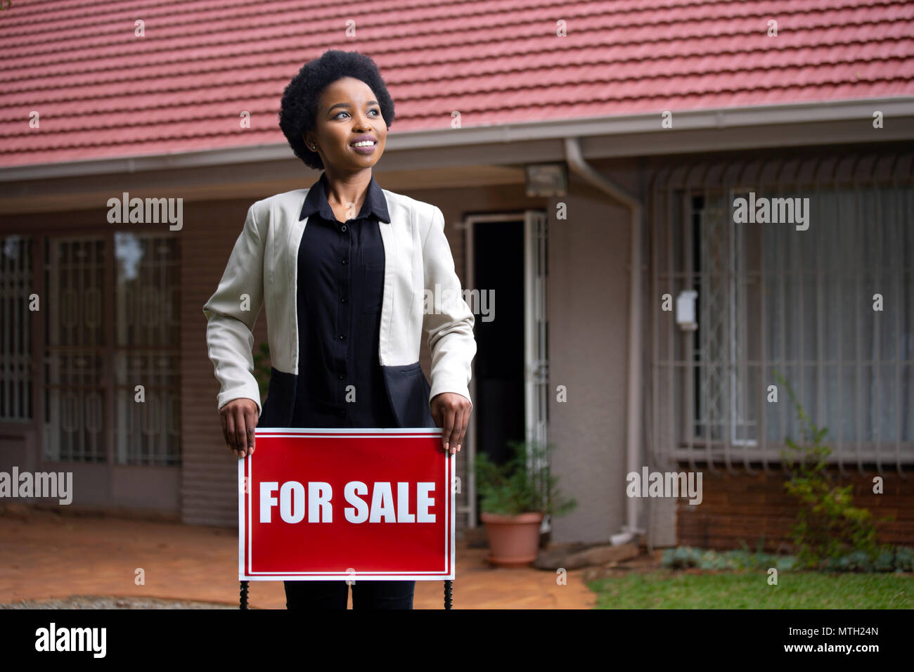 Estate agent holding For Sale sign in front of house Stock Photo
