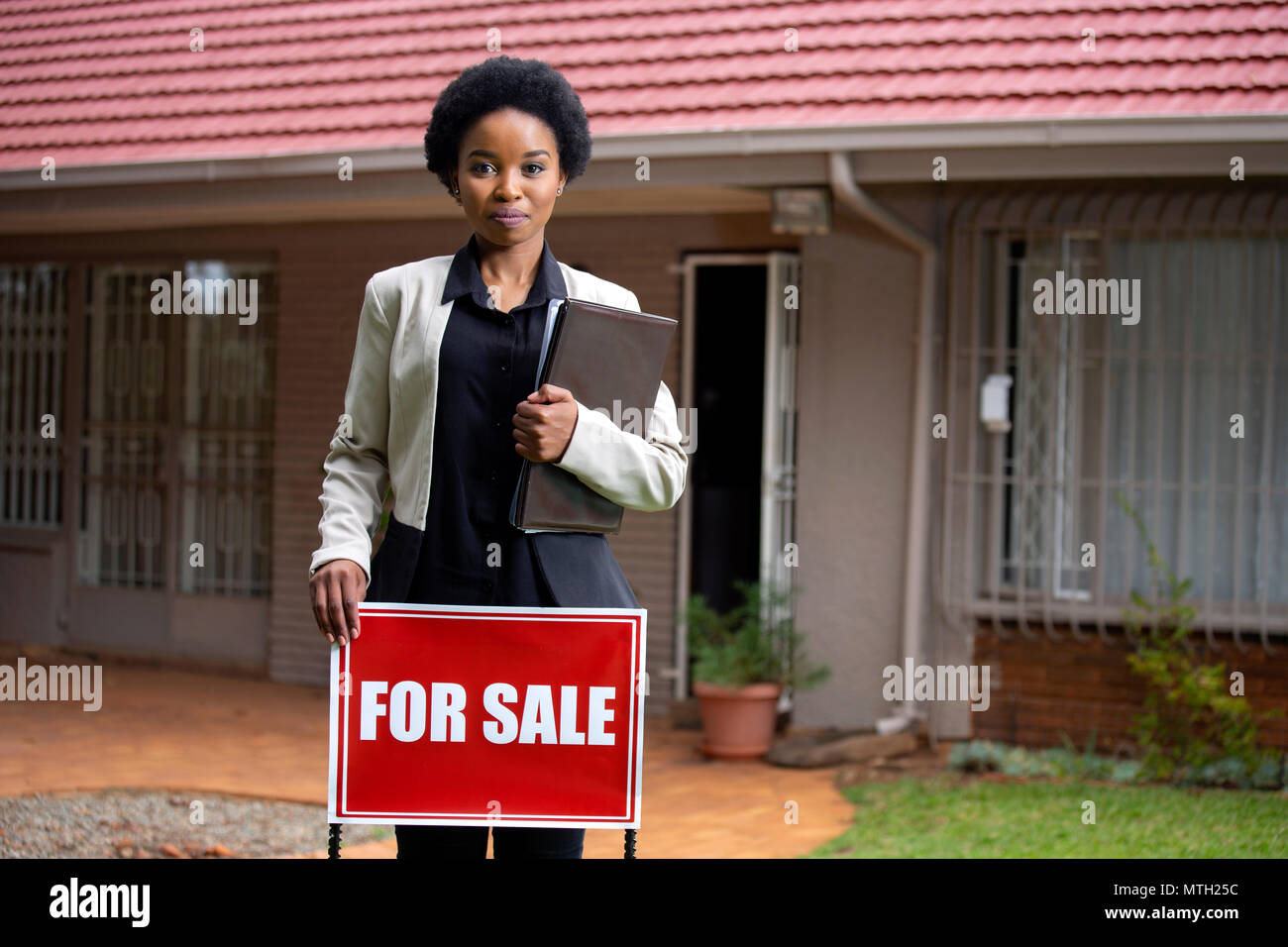 Estate agent holding For Sale sign and files  in front of house Stock Photo