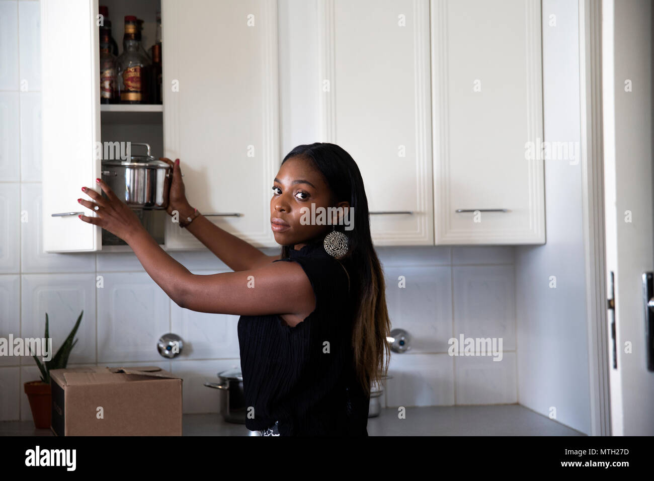 Woman putting pot into kitchen cupboard Stock Photo