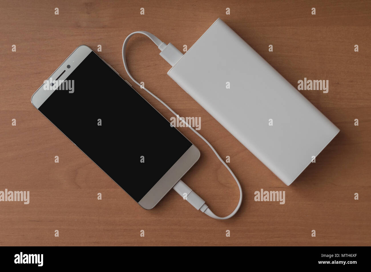 A modern smartphone and a connected power bank on a wooden background. Stock Photo