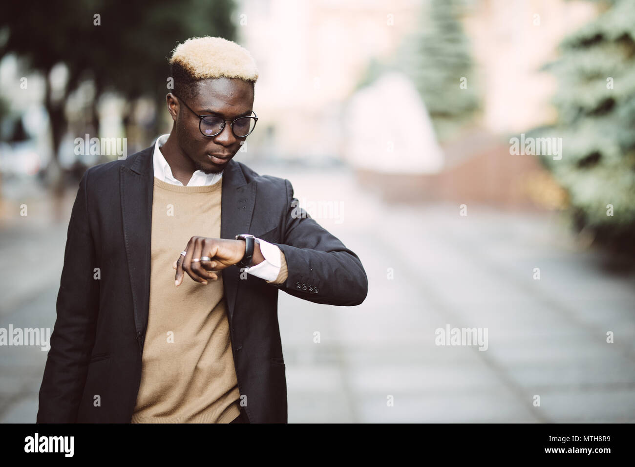 Handsome Afro American man looking at watch wearing suit in modern ...