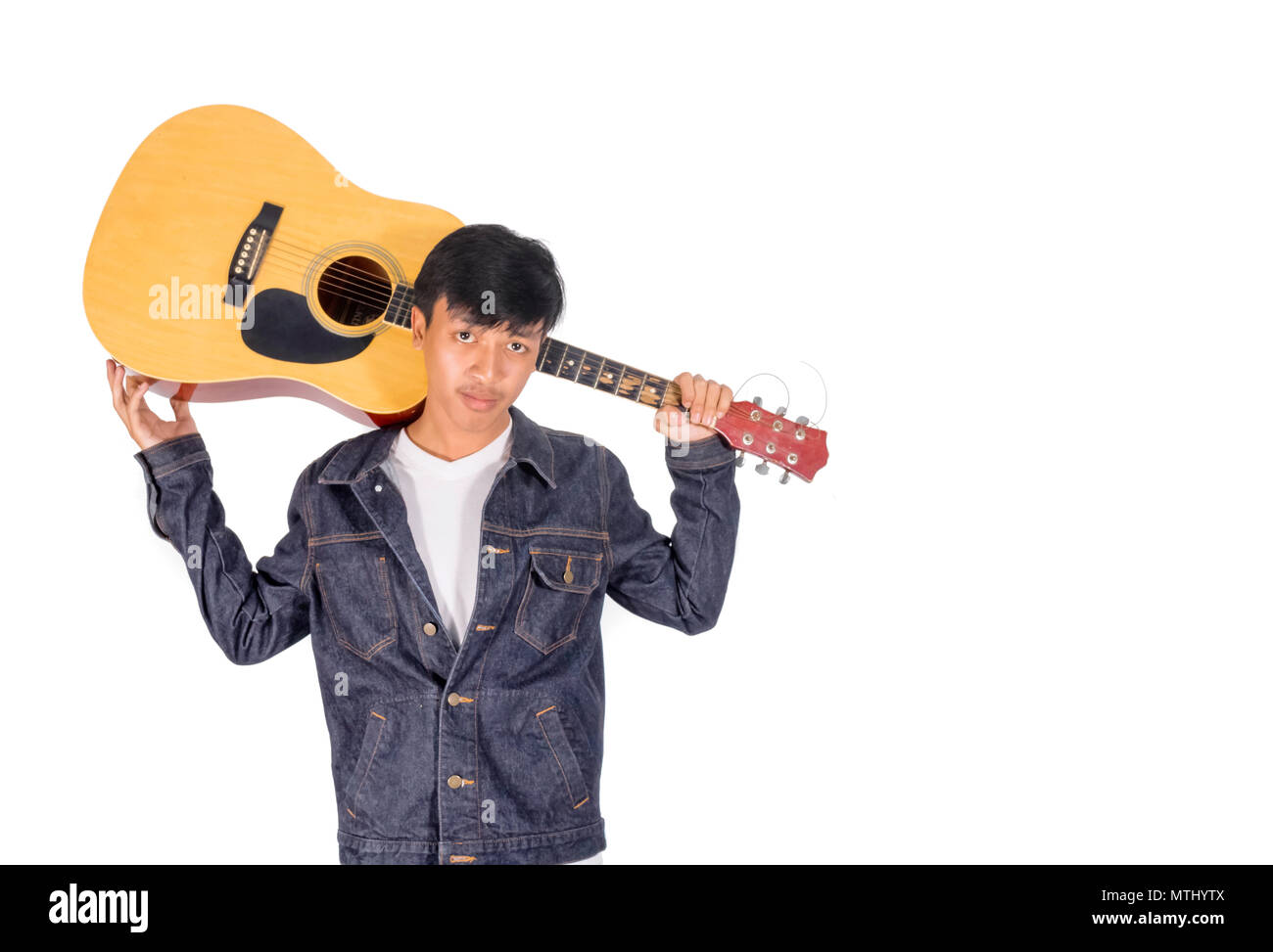 A portrait of an Asian man in blue jeans jacket is bearing an old guitar copy space. Stock Photo