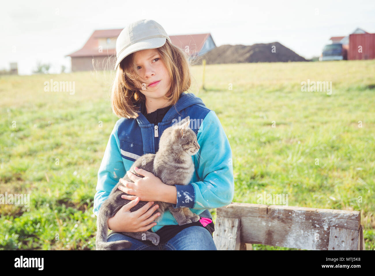 Girl child / tween holding pet cat (grey tabby kitten) protectively on building construction site whilst looking deep in thought Stock Photo