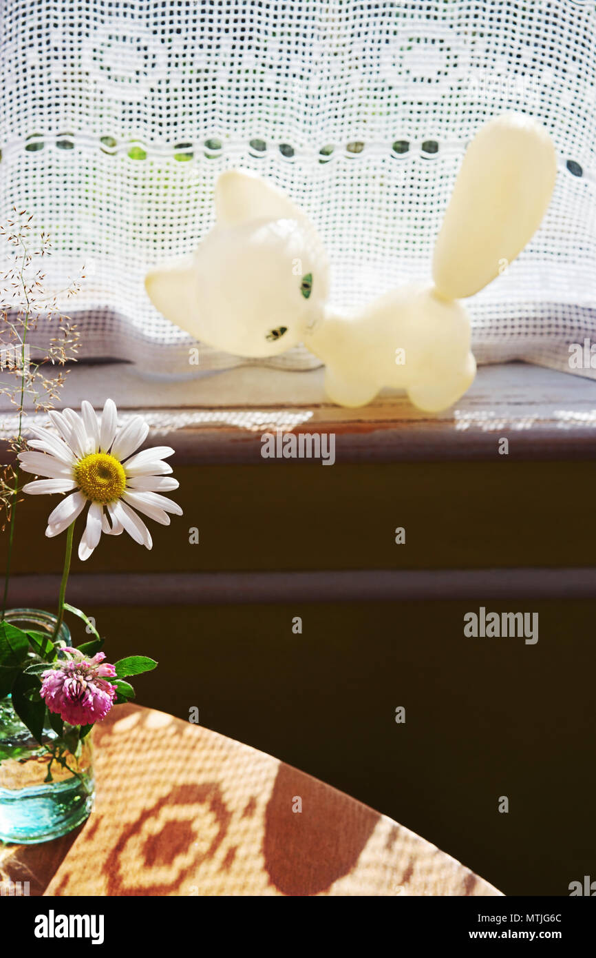 Chamomile on the glass and vintage toy white cat on the window sill Stock Photo