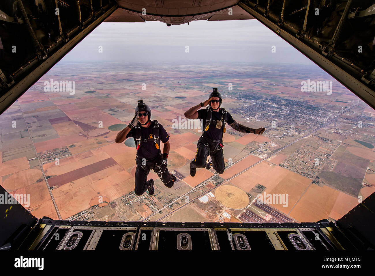 Two members of the U.S. Special Operations Command Para-Commandos salute as the jump out of a MC-130J Commando II aircraft during the Cannon Air Show, Space and Tech Fest at Cannon Air Force Base, N.M., May 26, 2018. The Para-Commandos are the only DoD Joint Service demonstration team consisting of members from every Military Service in SOCOM. (U.S. Air Force photo by Senior Airman Luke Kitterman/Released) Stock Photo