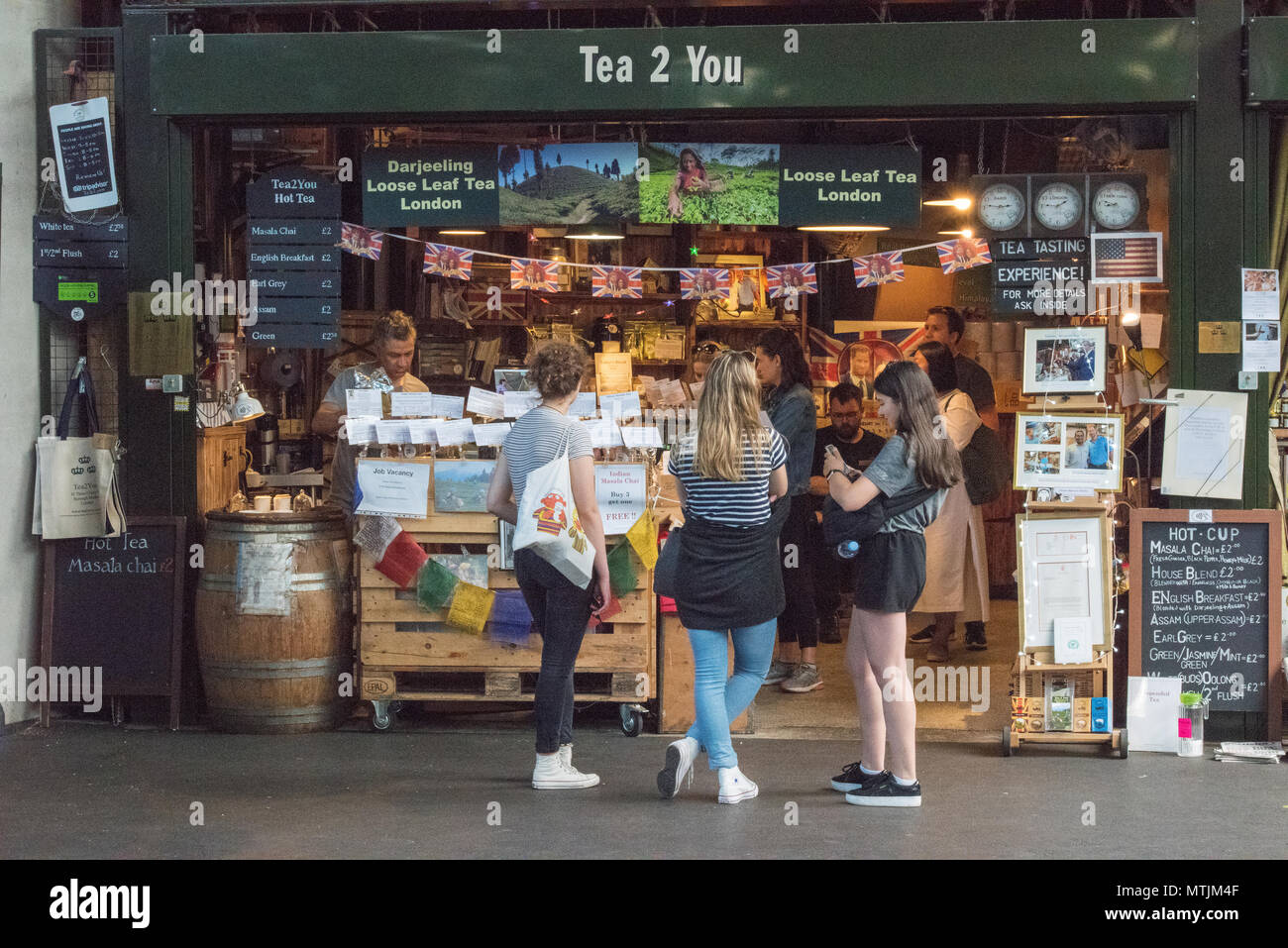 three young women or girls standing outside of a tea shop or stall