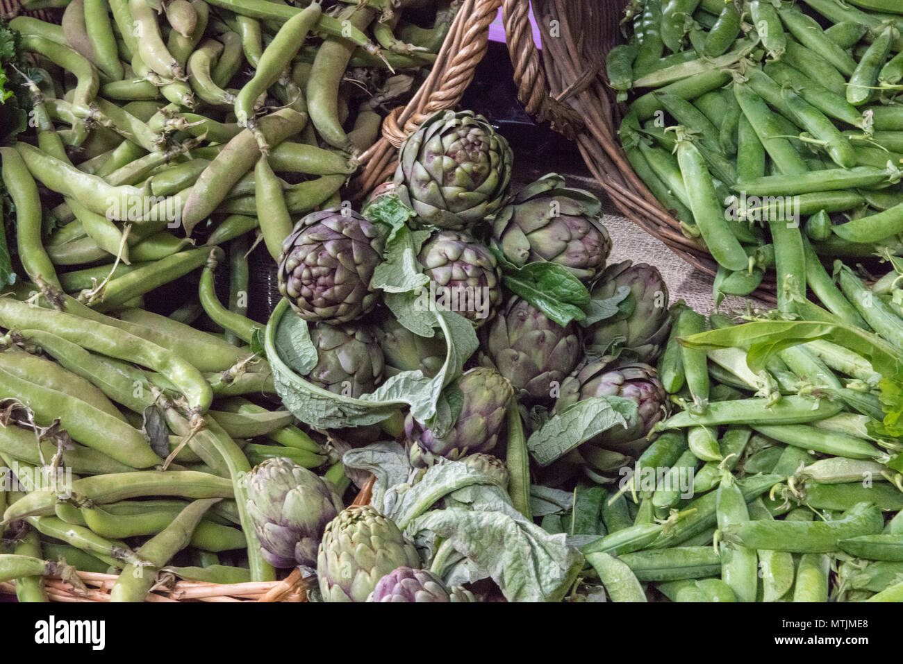 fresh artichokes and green pea pods o display at borough market greengrocers stall on a market. Stock Photo