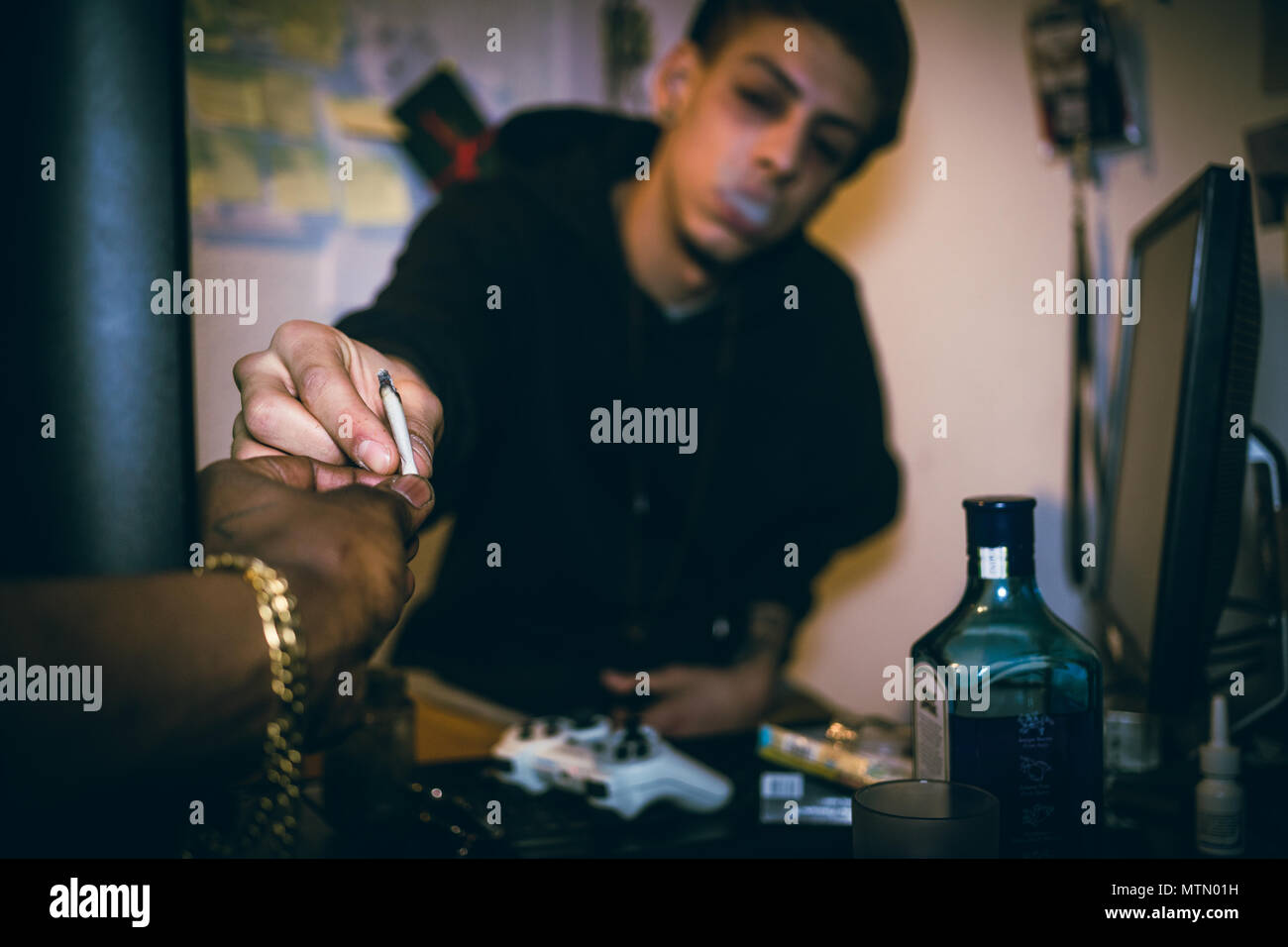 Close-up of the hands of two drug addicted young men or teenage boys sharing a marijuana joint at home in a dark room Stock Photo