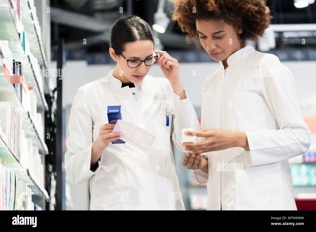 Low-angle view of two reliable pharmacists analyzing together a medical prescription and two different packages of medicine during work in a modern dr Stock Photo